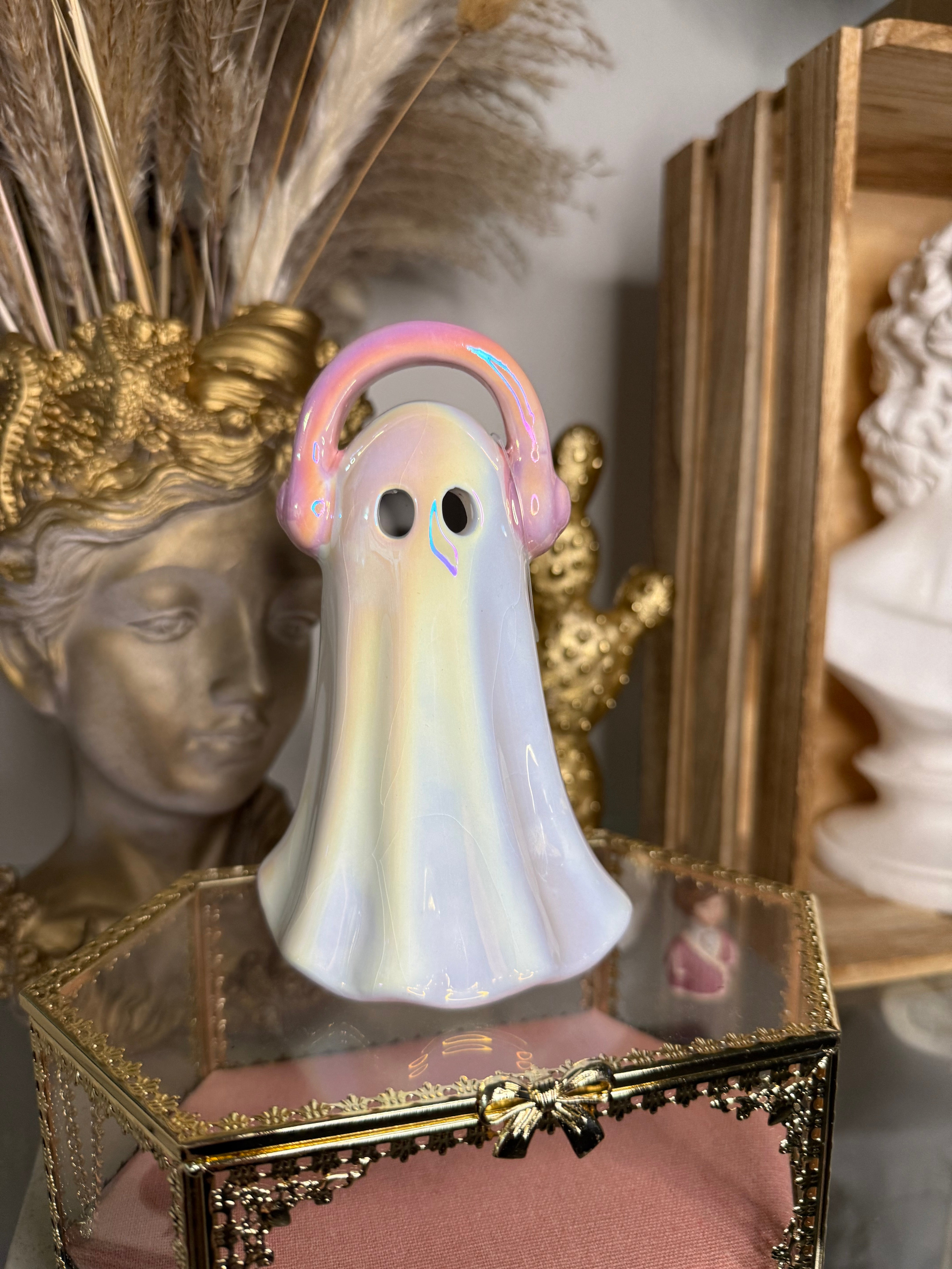 Decorative ghost-shaped object with pink headphone in front of a gold frame.