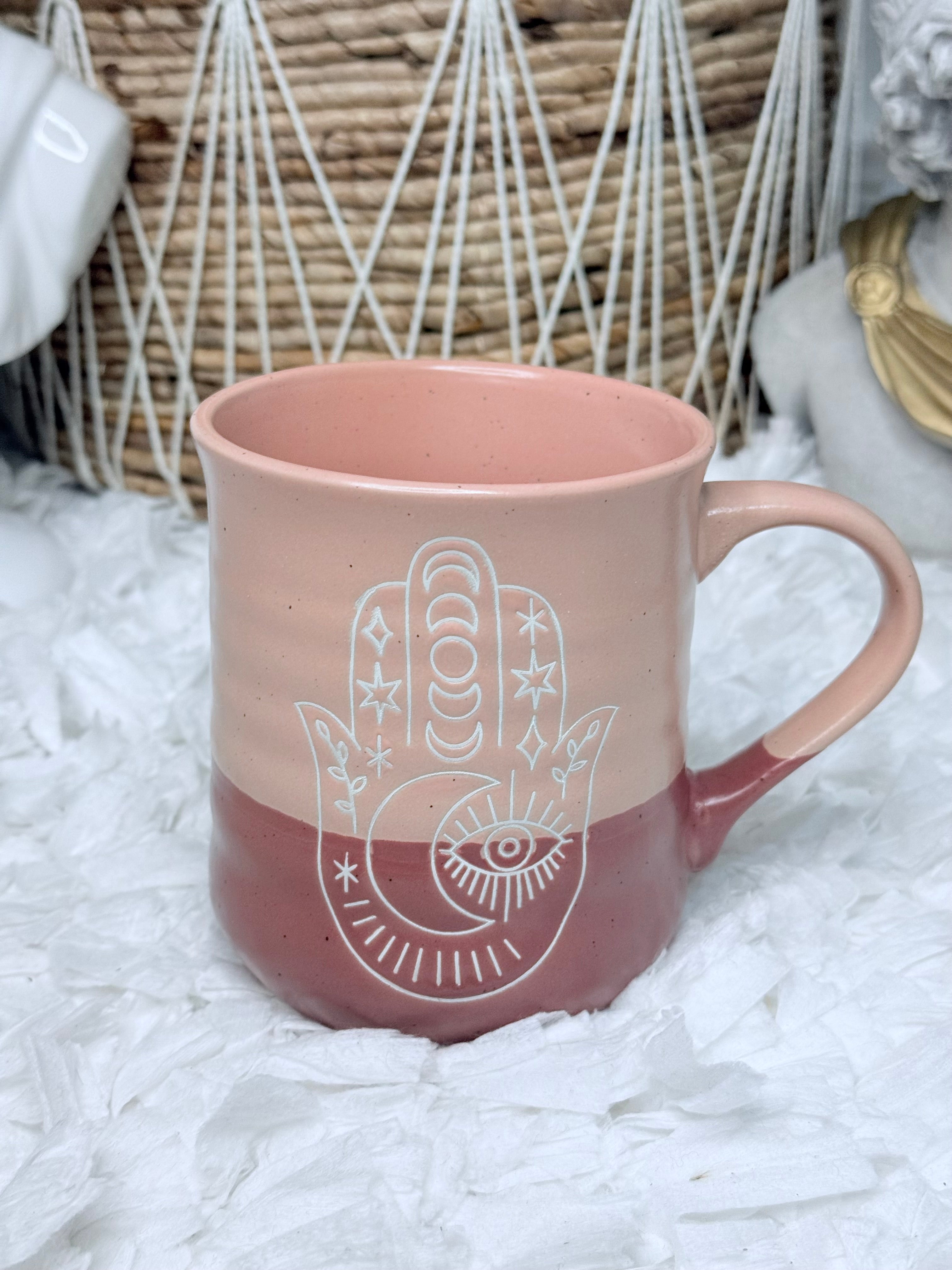 Blush pink ceramic mug featuring engraved Hamsa and all-seeing eye symbol, perfect for boho spiritual kitchen décor.