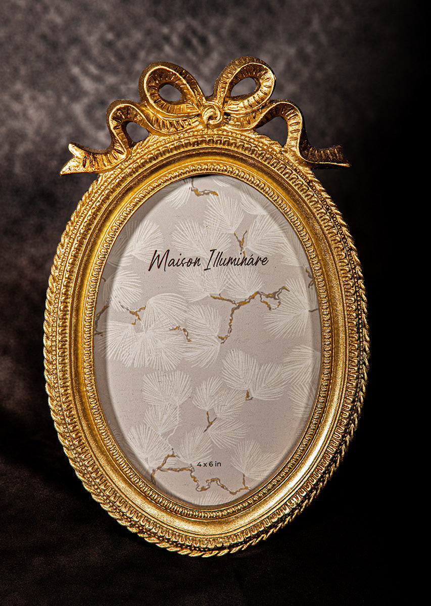 Antique gold oval picture frame with bow detail, vintage Hollywood Regency style.
