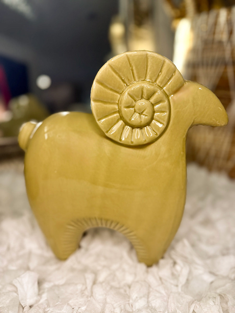 Mustard-chartreuse ceramic ram figurine, side view; modern Aries decor on a textured cream rug with blurred background.