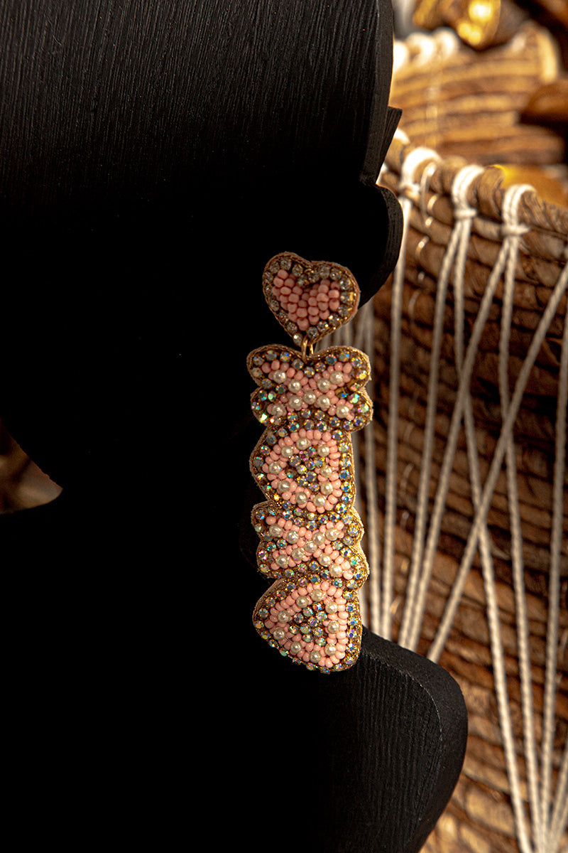 Decorative earring with pink beads on a black stand against a woven background