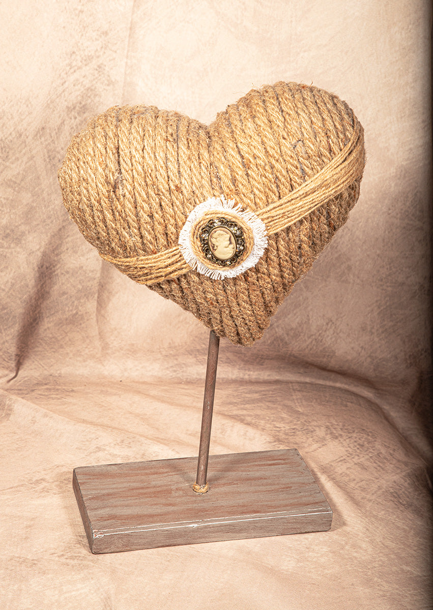 Heart-shaped object made of rope on a stand with a beige background.