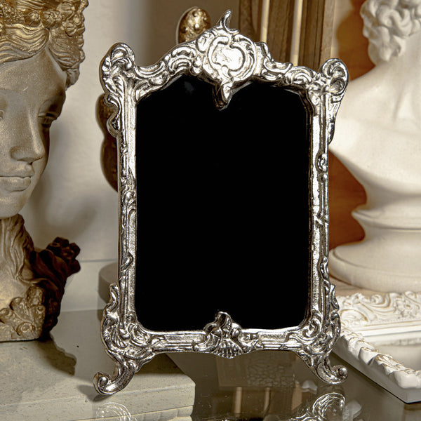 Decorative silver frame with black center on a reflective surface with classical sculptures in the background.