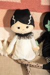 Plush toy with black hair and white outfit on a textured surface