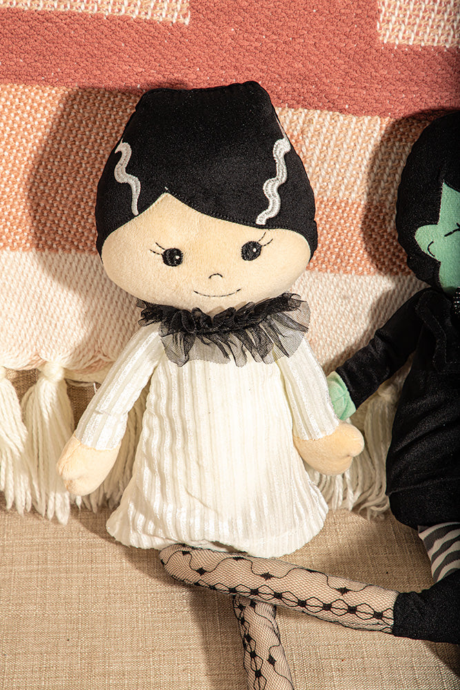 Plush toy with black hair and white outfit on a textured surface