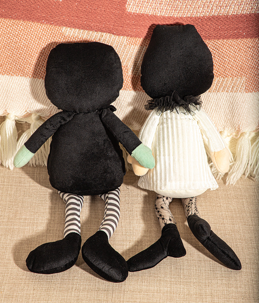 Two black hooded dolls with striped socks and green gloves on a textured surface.