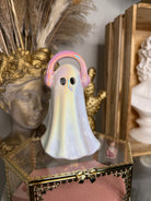 Decorative ghost-shaped object with pink headphone in front of a gold frame.