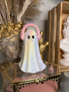 Decorative ghost-shaped object with pink headphone in front of a gold frame.