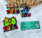 Colorful tequila-themed pins with a humorous Mexican road sign on a textured white background.