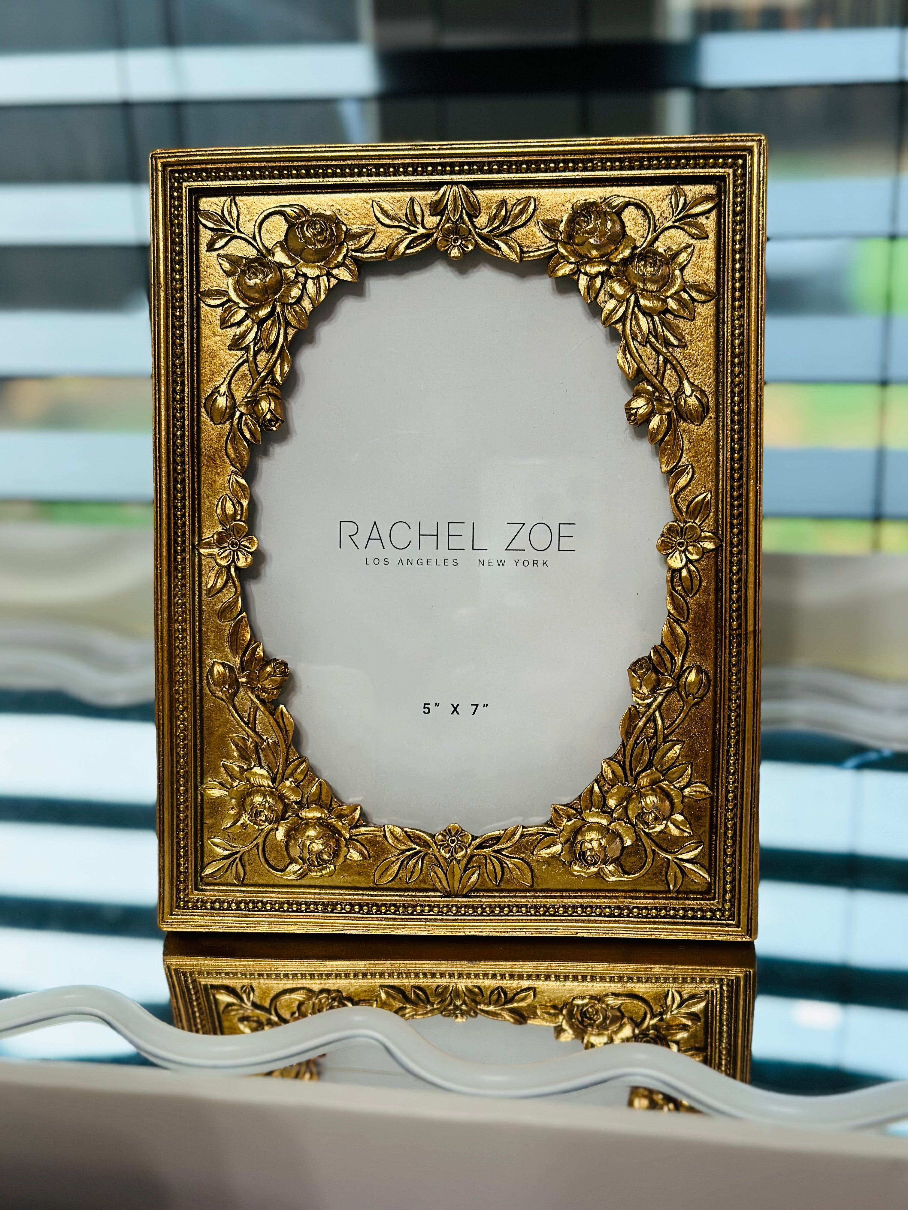 Ornate baroque gold rectangular picture frame with raised floral corners, 5x7 opening, displayed on a mirrored vanity.