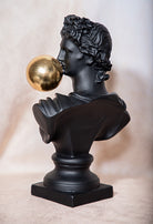 Bust of a classical figure with a gold ball on a beige background