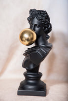 Black bust with a gold bubblegum ball on a beige background
