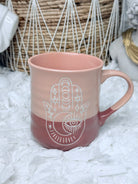 Blush pink ceramic mug featuring engraved Hamsa and all-seeing eye symbol, perfect for boho spiritual kitchen décor.
