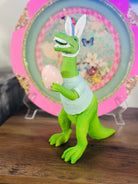 Green T-rex dinosaur holding pink polka dot egg, whimsical Easter decor piece.