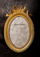 Antique gold oval picture frame with bow detail, vintage Hollywood Regency style.
