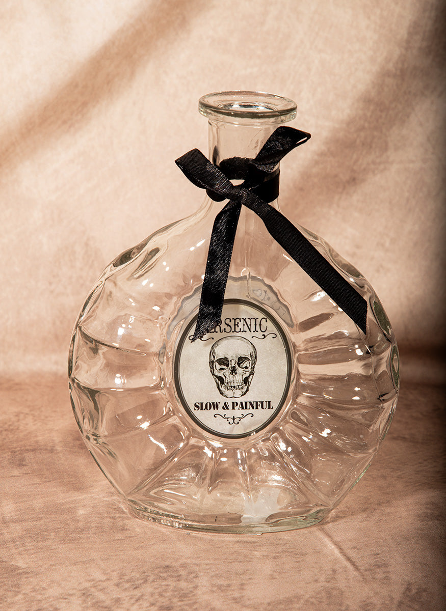 Clear glass bottle with a black ribbon and skull label on a wooden surface