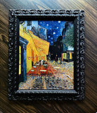 Ornate black baroque frame featuring textured Van Gogh Café Terrace at Night canvas art on dark wood background.