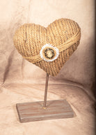 Heart-shaped object made of rope on a stand with a beige background.