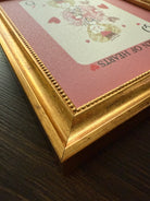 Framed card with 'Queen of Hearts' design on a wooden surface